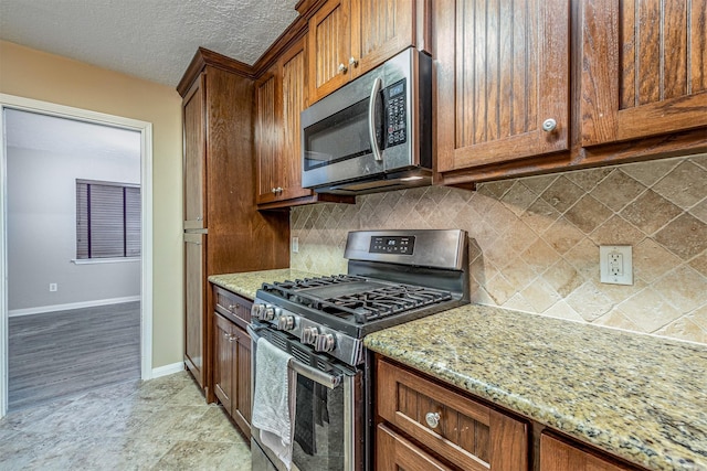 kitchen featuring light stone counters, decorative backsplash, stainless steel appliances, and a textured ceiling