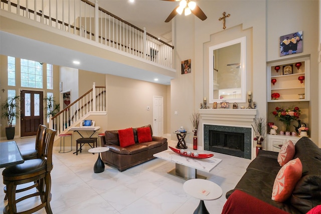 living room featuring a high end fireplace, ceiling fan, and a high ceiling