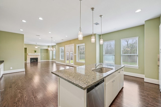 kitchen featuring an island with sink, open floor plan, stainless steel dishwasher, white cabinetry, and a sink