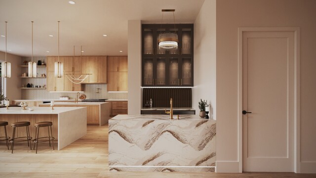 kitchen featuring sink, backsplash, a kitchen breakfast bar, hanging light fixtures, and light hardwood / wood-style floors