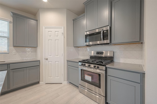 kitchen with light hardwood / wood-style flooring, backsplash, gray cabinets, and appliances with stainless steel finishes