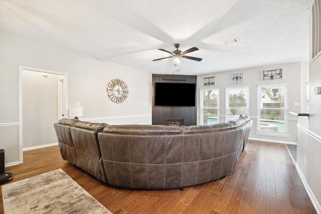 living room featuring ceiling fan, dark wood-type flooring, and a textured ceiling