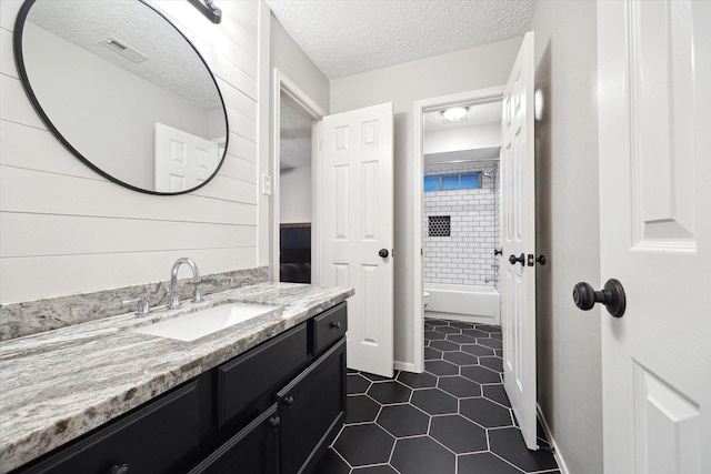 full bathroom with tile patterned flooring, vanity, tiled shower / bath combo, toilet, and a textured ceiling