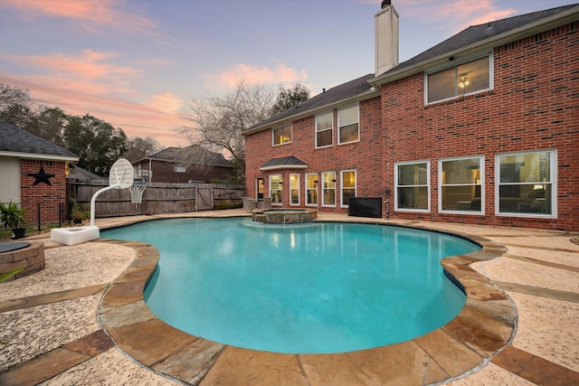 pool at dusk with an in ground hot tub and a patio