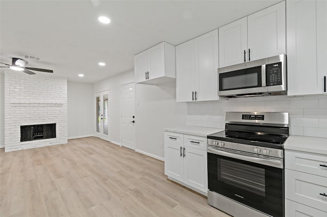 kitchen featuring white cabinets, backsplash, stainless steel appliances, a brick fireplace, and light wood-type flooring