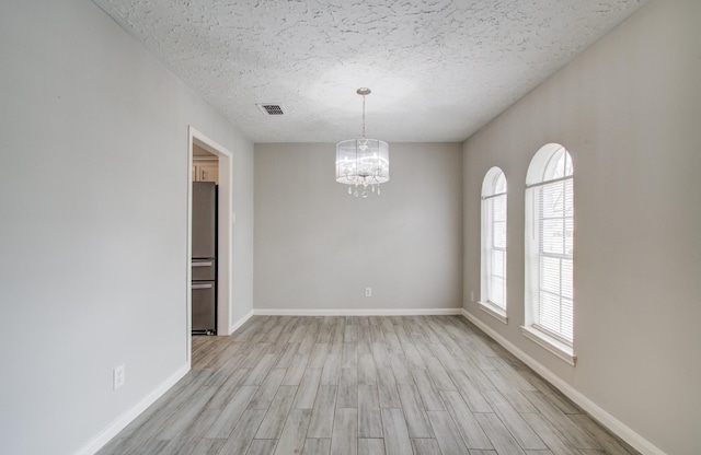 unfurnished room featuring an inviting chandelier, light hardwood / wood-style flooring, and a textured ceiling