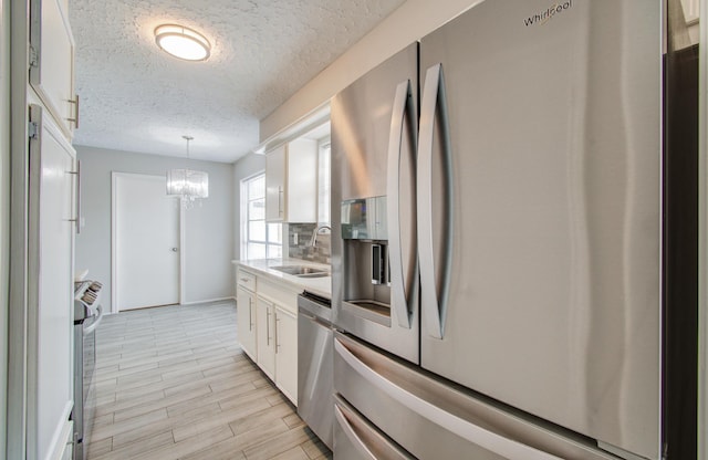 kitchen featuring sink, white cabinetry, pendant lighting, stainless steel appliances, and backsplash