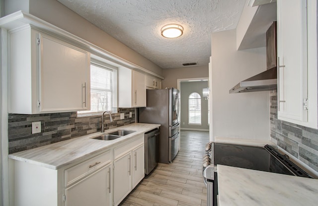 kitchen with sink, white cabinetry, appliances with stainless steel finishes, light hardwood / wood-style floors, and wall chimney range hood