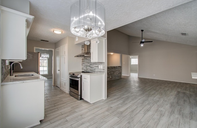 kitchen featuring ceiling fan with notable chandelier, sink, white cabinets, stainless steel range with electric cooktop, and wall chimney range hood