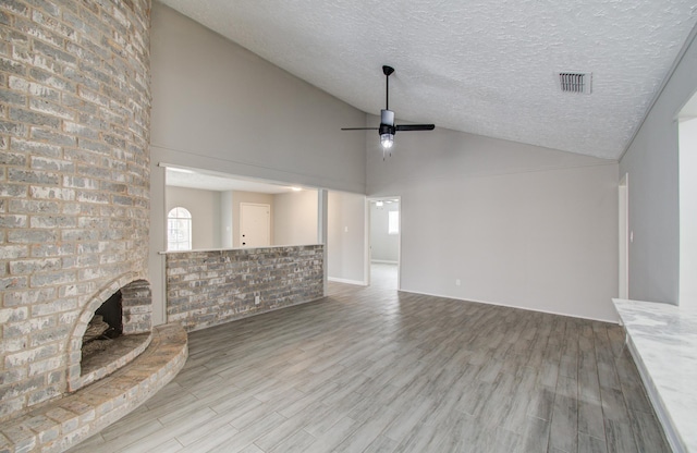 unfurnished living room featuring lofted ceiling, a textured ceiling, a brick fireplace, light wood-type flooring, and ceiling fan