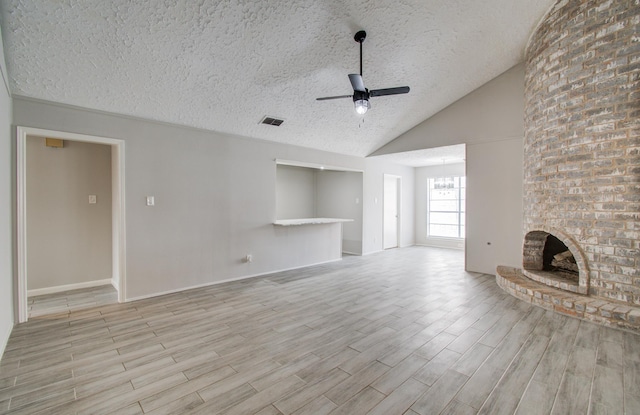 unfurnished living room featuring a fireplace, light hardwood / wood-style floors, a textured ceiling, ceiling fan with notable chandelier, and vaulted ceiling