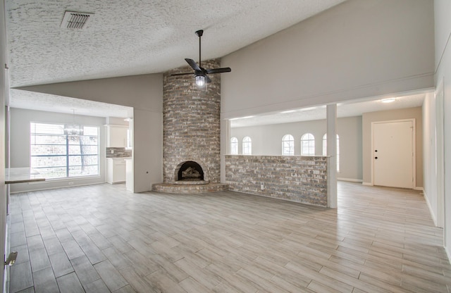 unfurnished living room featuring ceiling fan with notable chandelier, a fireplace, high vaulted ceiling, and a textured ceiling