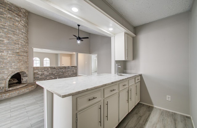 kitchen with lofted ceiling, sink, a brick fireplace, kitchen peninsula, and light stone countertops