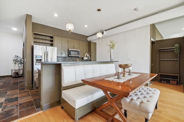 kitchen featuring tasteful backsplash, hanging light fixtures, light hardwood / wood-style floors, kitchen peninsula, and stainless steel appliances