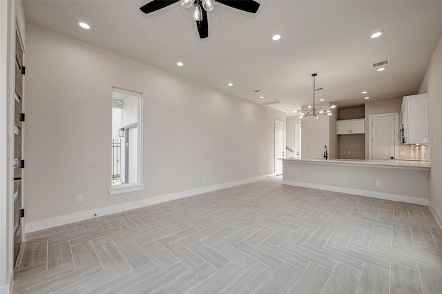 unfurnished living room featuring ceiling fan with notable chandelier and light parquet flooring