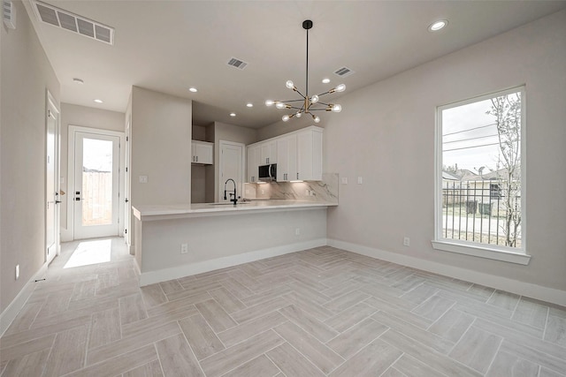 kitchen with decorative light fixtures, tasteful backsplash, white cabinetry, sink, and kitchen peninsula