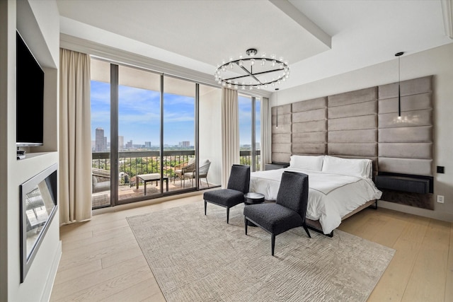 bedroom with a chandelier, light hardwood / wood-style flooring, access to outside, a raised ceiling, and a wall of windows