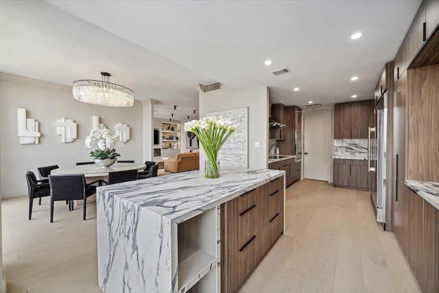 kitchen featuring tasteful backsplash, high end refrigerator, hanging light fixtures, light hardwood / wood-style floors, and light stone countertops