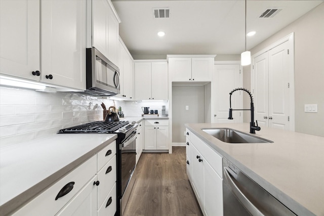 kitchen with sink, appliances with stainless steel finishes, white cabinets, dark hardwood / wood-style floors, and pendant lighting