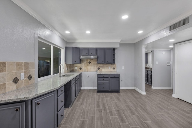 kitchen with sink, light stone counters, crown molding, gray cabinets, and backsplash