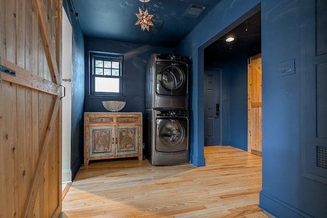 washroom featuring a barn door, wood-type flooring, and stacked washer and clothes dryer