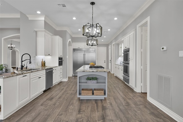 kitchen featuring stainless steel appliances, white cabinets, light stone counters, and decorative light fixtures