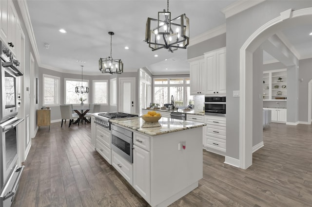 kitchen featuring appliances with stainless steel finishes, white cabinets, a chandelier, a center island, and light stone counters