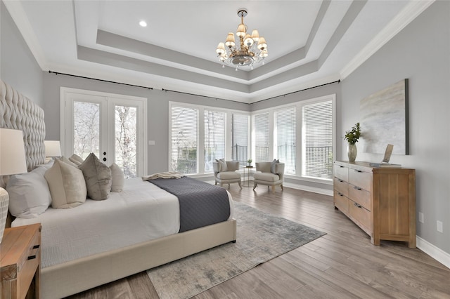 bedroom featuring french doors, an inviting chandelier, access to outside, a tray ceiling, and light hardwood / wood-style floors