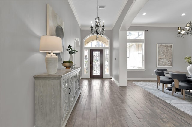 foyer featuring wood-type flooring, ornamental molding, and a notable chandelier