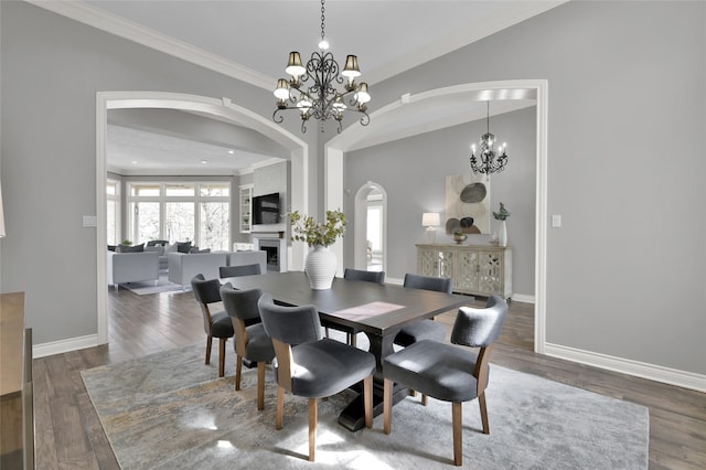 dining space featuring a large fireplace, ornamental molding, dark hardwood / wood-style flooring, and a notable chandelier