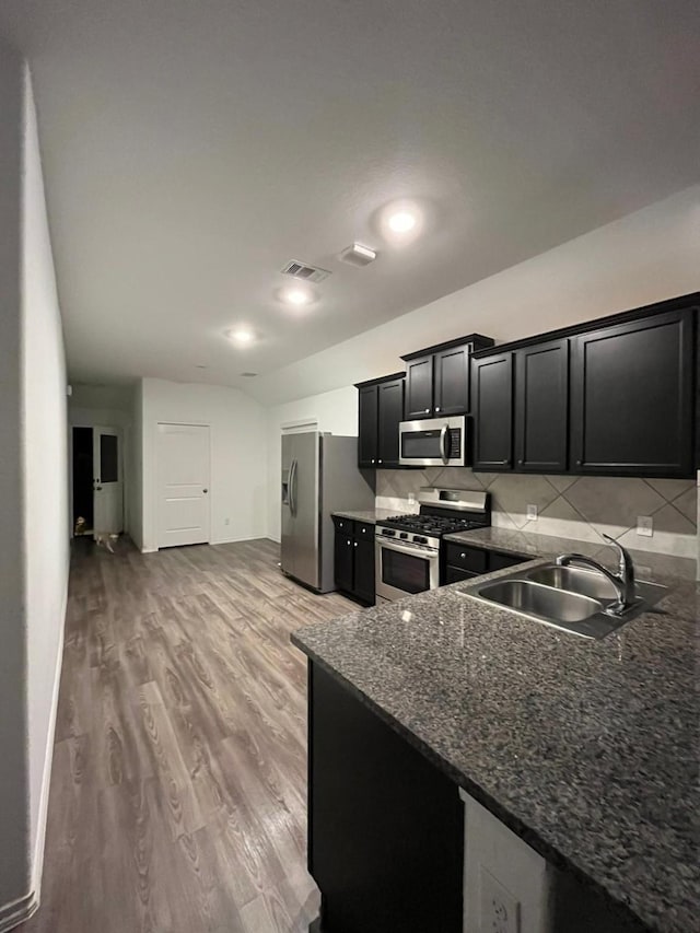 kitchen with sink, wood-type flooring, dark stone countertops, appliances with stainless steel finishes, and backsplash