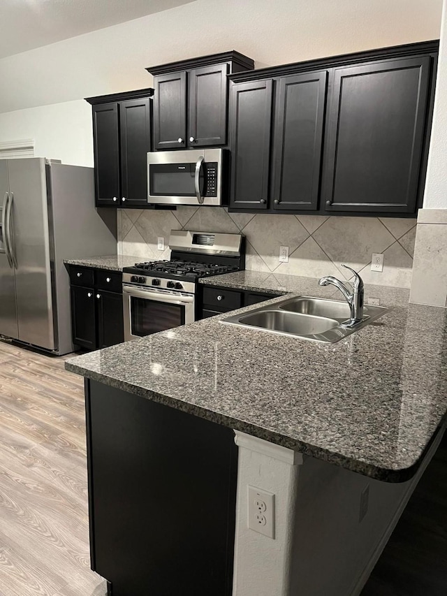 kitchen featuring sink, backsplash, dark stone counters, stainless steel appliances, and light hardwood / wood-style flooring