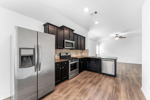 kitchen with kitchen peninsula, lofted ceiling, stainless steel appliances, dark hardwood / wood-style flooring, and decorative backsplash