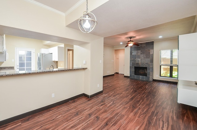 unfurnished living room featuring a tile fireplace, ornamental molding, dark wood-type flooring, and ceiling fan