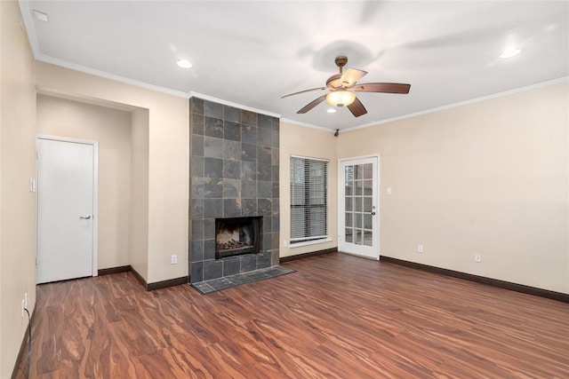 unfurnished living room featuring a tiled fireplace, crown molding, dark wood-type flooring, and ceiling fan