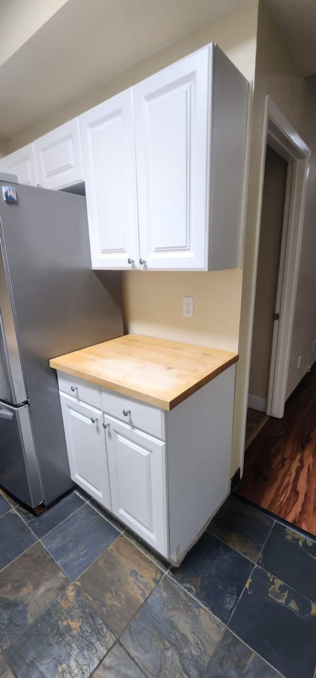 kitchen with butcher block countertops, white cabinets, and stainless steel refrigerator