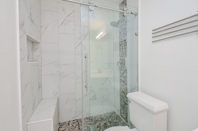 bathroom featuring a shower with door and toilet