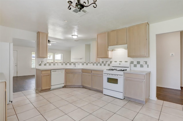 kitchen featuring light brown cabinetry, white appliances, under cabinet range hood, and a sink