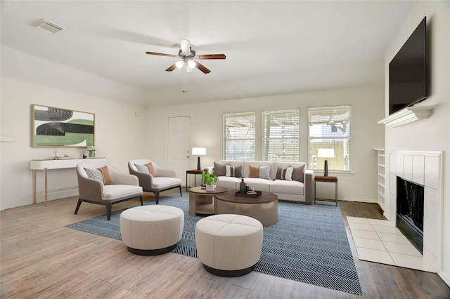 living area with visible vents, a fireplace, a ceiling fan, and wood finished floors