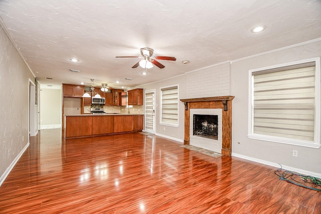 unfurnished living room featuring wood-type flooring, ornamental molding, ceiling fan, a brick fireplace, and a textured ceiling