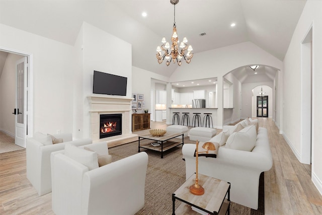 living room with light wood finished floors, arched walkways, a glass covered fireplace, high vaulted ceiling, and recessed lighting