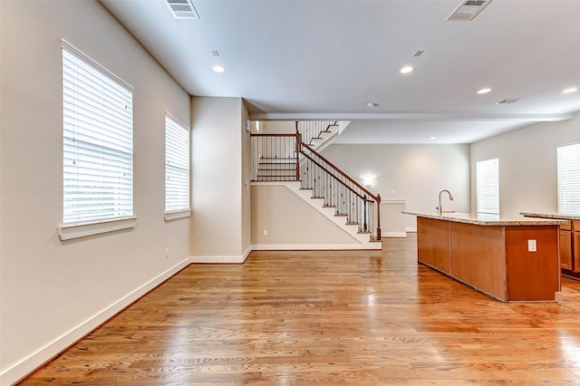 interior space featuring light stone countertops, a healthy amount of sunlight, a center island with sink, and light hardwood / wood-style flooring