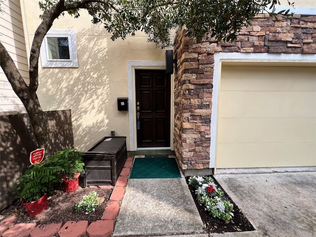 entrance to property with a garage, stone siding, and stucco siding