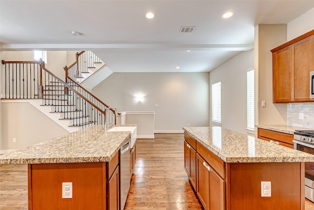 kitchen with a center island, appliances with stainless steel finishes, light stone countertops, light hardwood / wood-style floors, and decorative backsplash