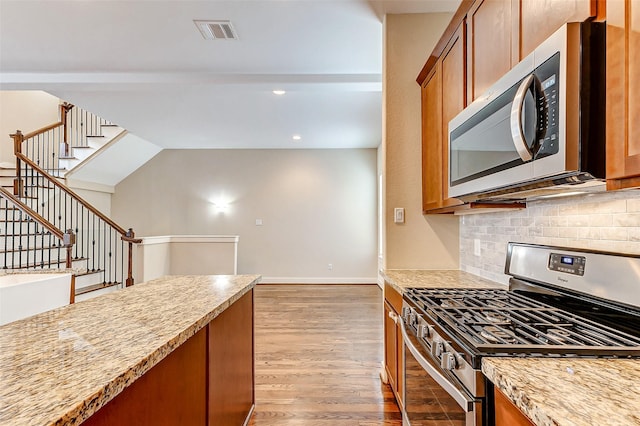 kitchen featuring light stone counters, stainless steel appliances, hardwood / wood-style floors, and decorative backsplash