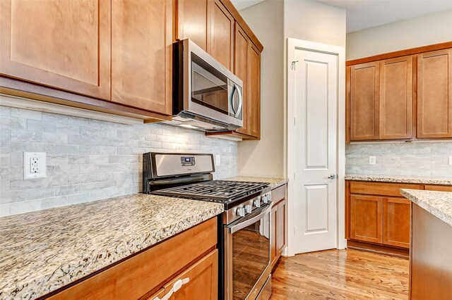 kitchen featuring light stone counters, stainless steel appliances, tasteful backsplash, and light wood-type flooring