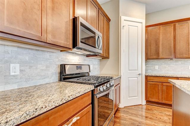 kitchen featuring decorative backsplash, light stone countertops, stainless steel appliances, and light wood finished floors