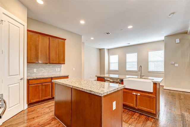 kitchen featuring tasteful backsplash, sink, a kitchen island with sink, and light wood-type flooring