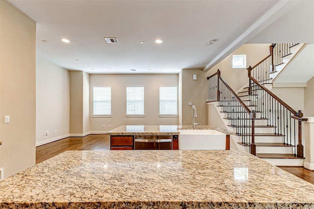 kitchen with a kitchen island, sink, dark hardwood / wood-style flooring, stainless steel dishwasher, and light stone counters