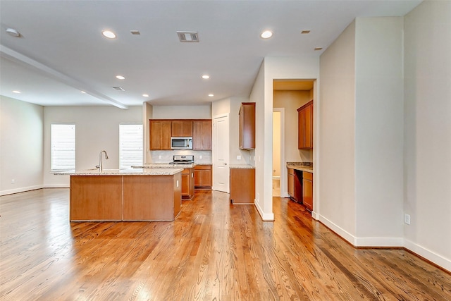 kitchen featuring sink, light stone counters, light hardwood / wood-style flooring, an island with sink, and stainless steel appliances